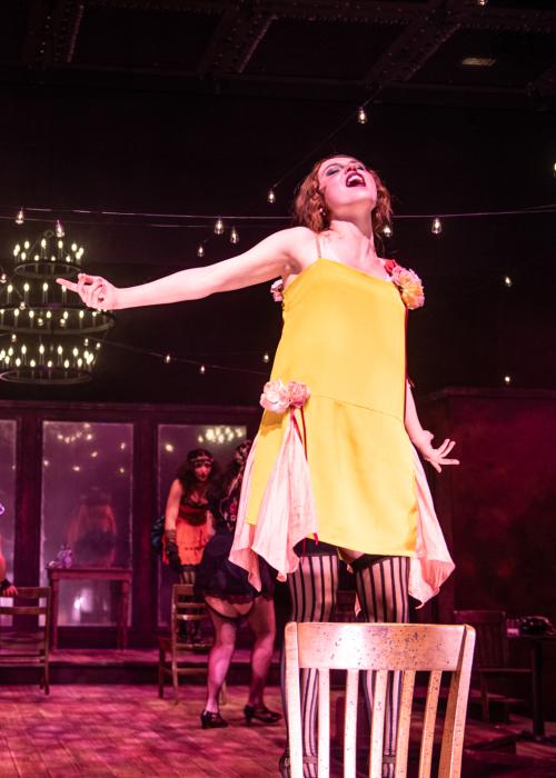 Actress singing on stage in Cabaret, there are dancers out of focus behind her