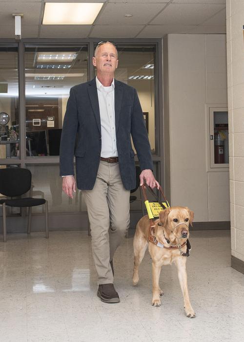 Jim Platzer and his leader dog are walking through a hallway