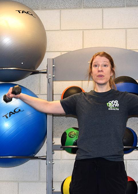 Female fitness instructor demonstrating side arm lifts holding weights for strength training class
