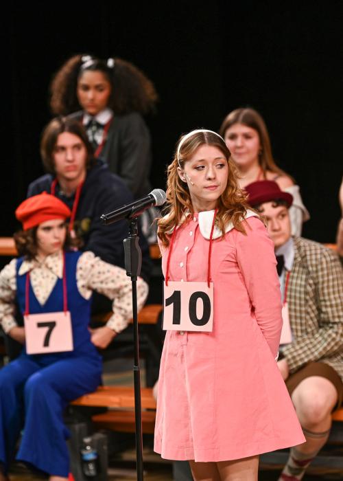 Several actors on stage performing as spelling bee contestants