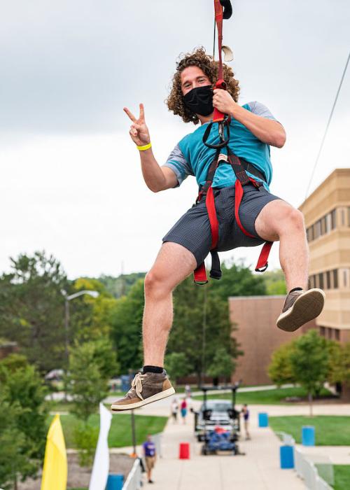 A student hangs from a zip line during campus kickoff