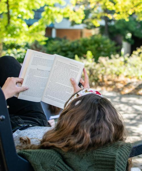 Student laying on a bench reading a book.
