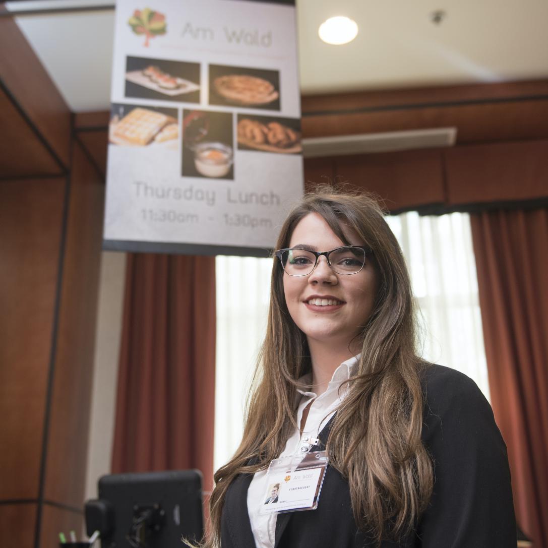 Hospitality student poses in from of a sign.