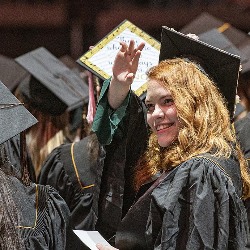 Student waves to friends in the audience at commencement.