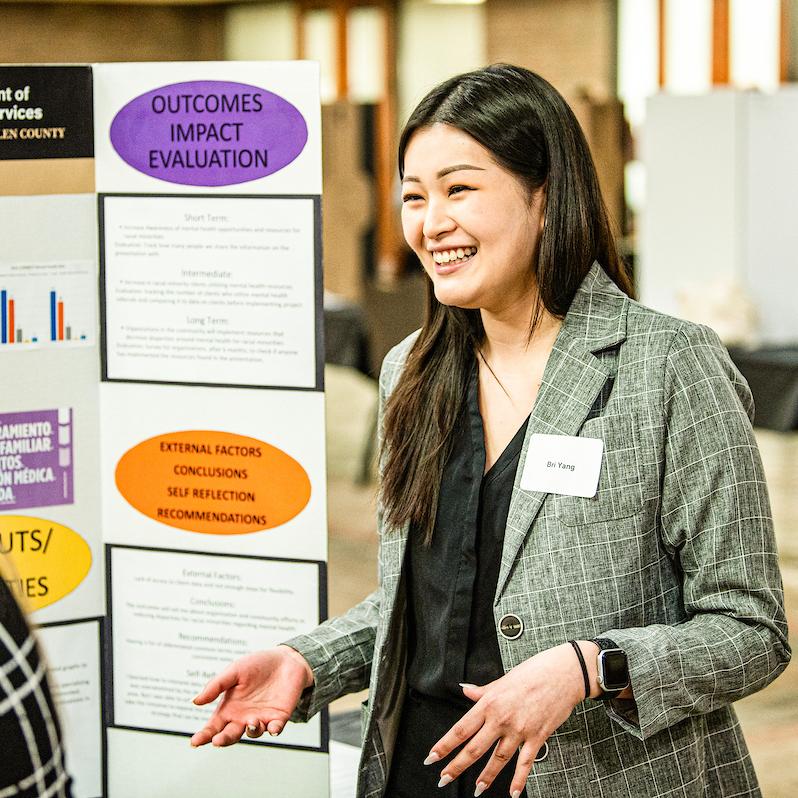 Student smiles while giving a poster presentation.