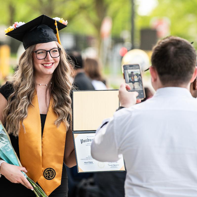 Graduate smiles for a photo holding flowers and their degree.