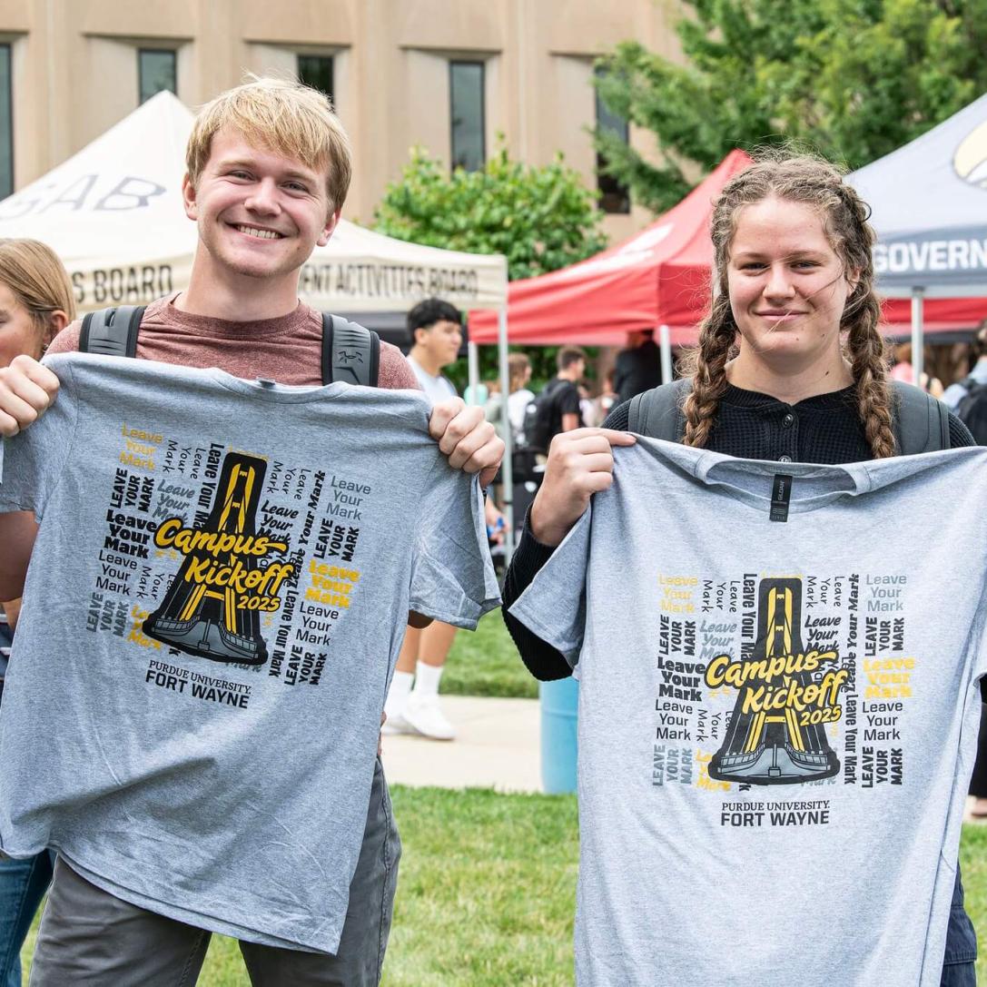 Two students are displaying campus kickoff t-shirts