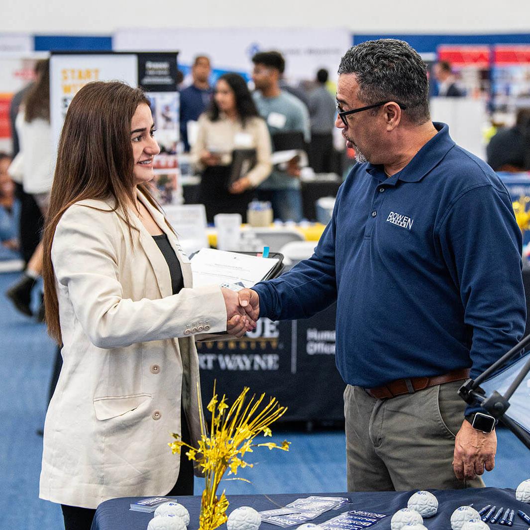 A student is shaking hands with a prospective employer at a career fair
