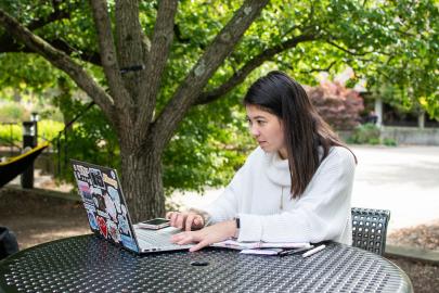 Student outdoors writing on a laptop.