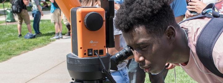 Student looks into a telescope at an eclipse party on campus.