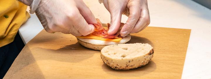 Shot of someone working in dining and putting together a breakfast bagel.