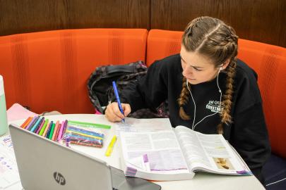 Student takes notes while reading a textbook in the library.