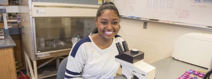 Biology student examining a slide sample on a lab microscope.