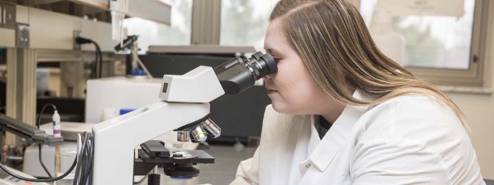 Biology student examining a slide sample on a lab microscope.