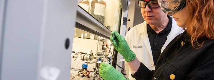 Chemistry professor explaining liquid sample gathering to a student in her research.