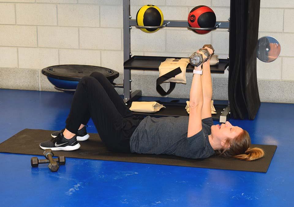 Health coach demonstrating arm press with small weights