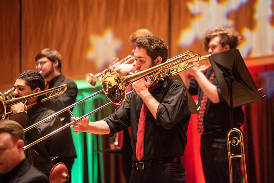 A group of students play brass instruments in front of a festive background.