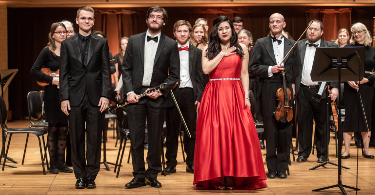 People standing on stage in tuxes and red dress