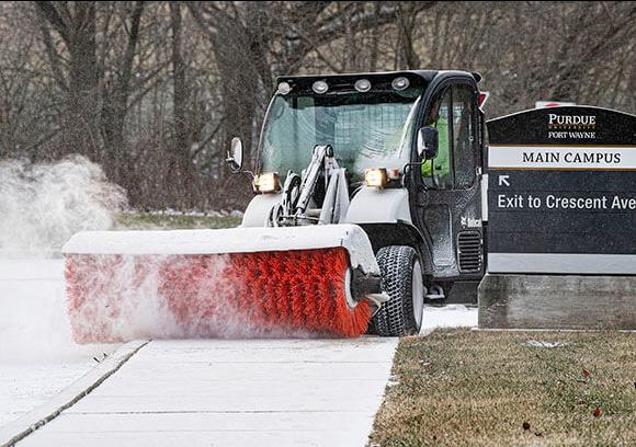 A grounds crew member is brushing the snow off of the sidewalk