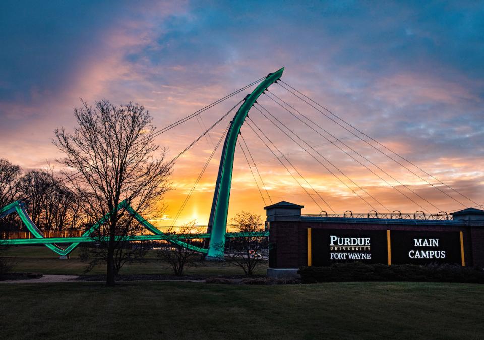 Campus sign with the bridge and a sunrise in the background.
