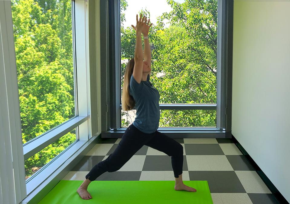 Health coach demonstrating warrior yoga pose with windowsshowing green leaves of trees