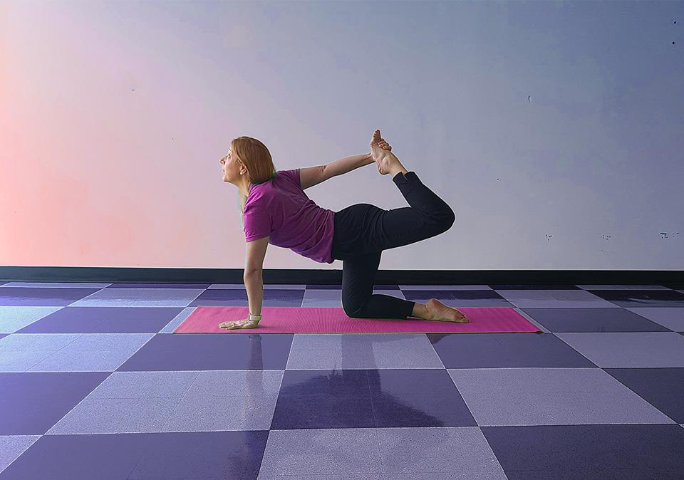 Female yoga instructor kneeling while using one hand to hold one of her feet behind her (modified dancer pose).