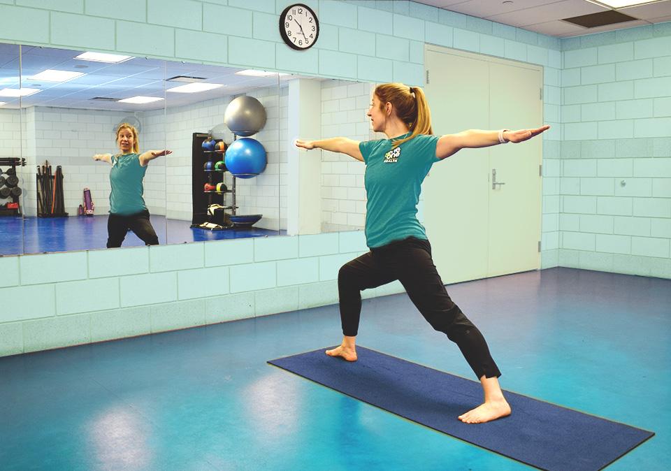 Female health coach on yoga mat demonstrating the warrior pose