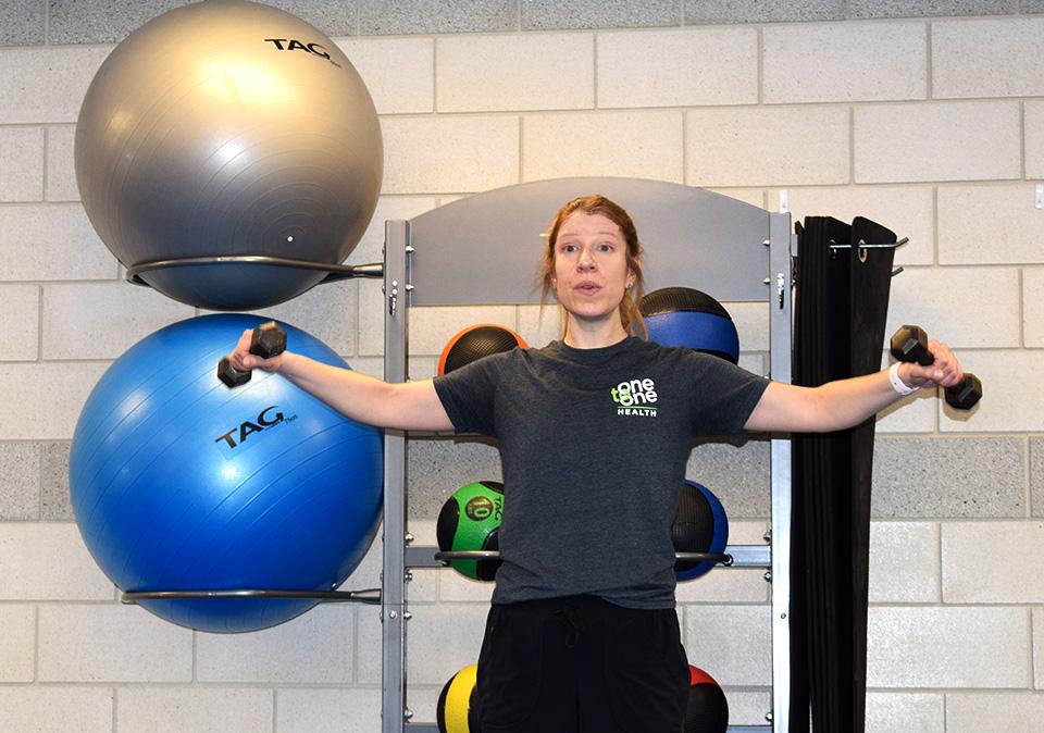 Female fitness instructor demonstrating side arm lifts holding weights for strength training class