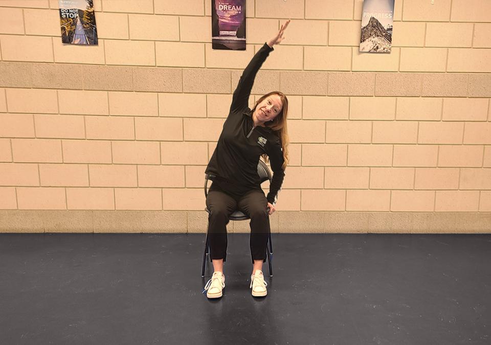 Chair yoga instructor showing how to do a side stretch shair yoga pose.