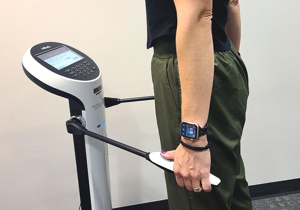 Woman using the InBody device which is like a standing scale that measures body composition.