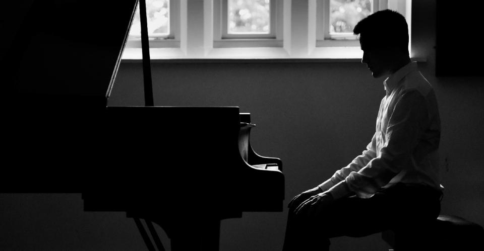 man sitting at piano in black and white