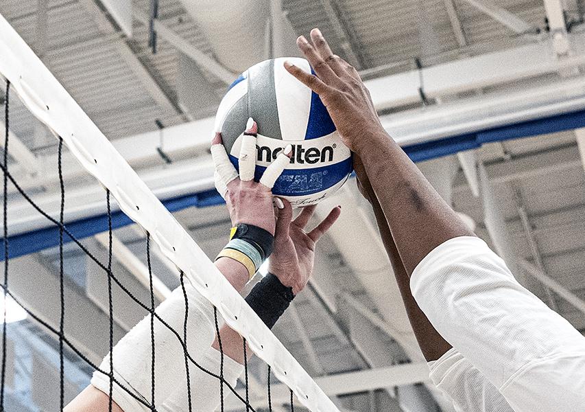 Two volleyball players are reaching for a volleyball