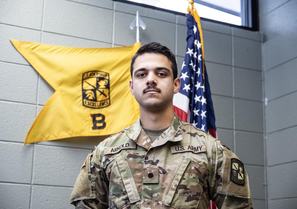 Tanis Arnold is wearing an Army uniform and standing in front of two flags