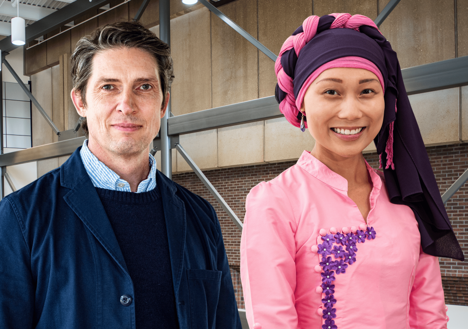 A man in a dark blue jacket and a woman in a pink outfit with a purple and pink headwrap stand side-by-side.