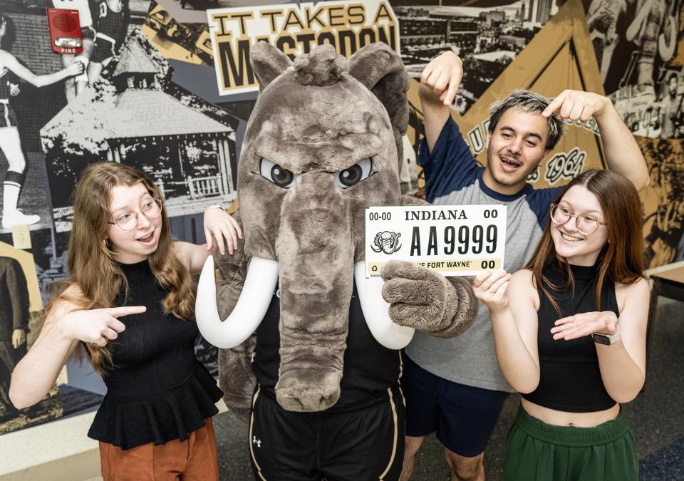 Three students pose with Don to show off a PFW license plate