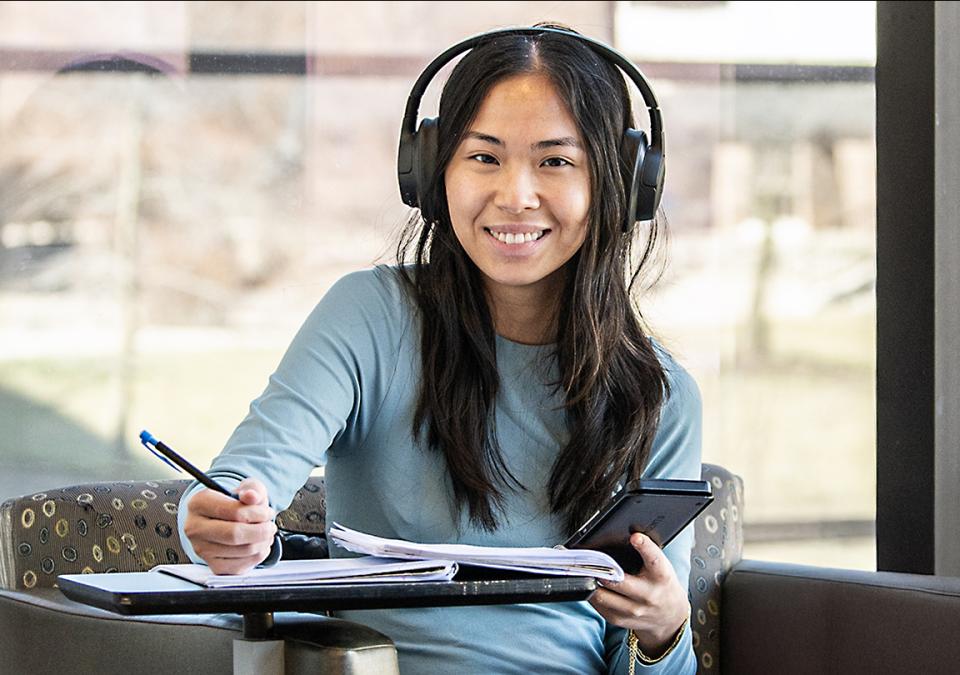 A student with headphones smiles while taking notes.