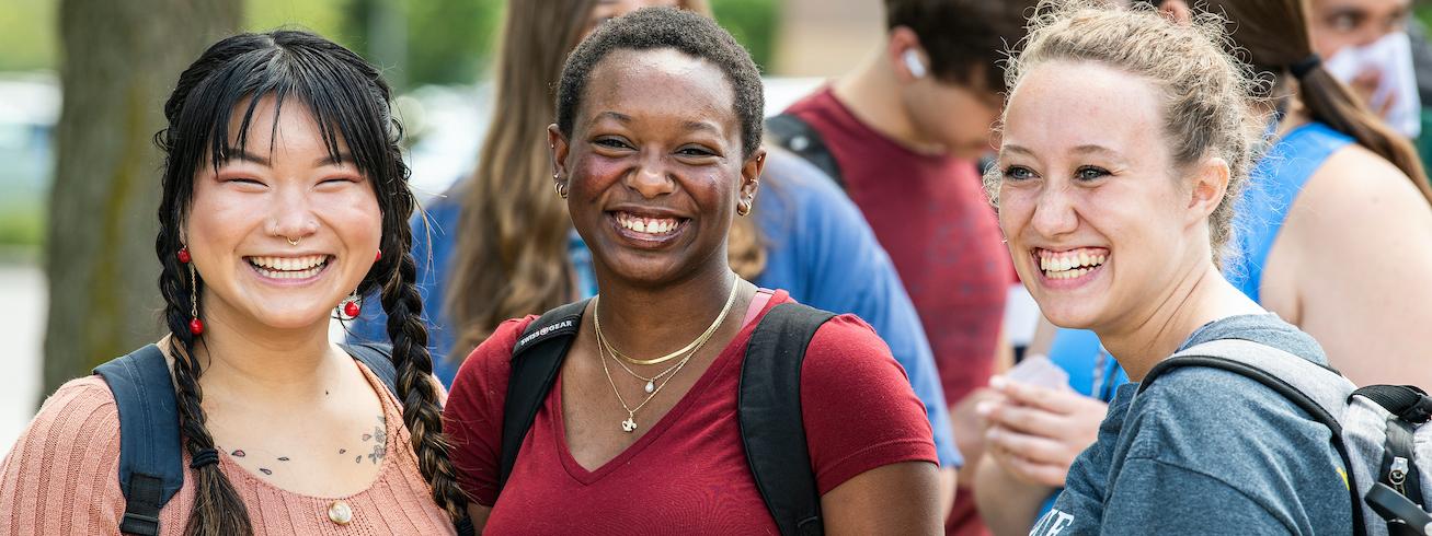 Students with backpacks on outside smiling for the camera.