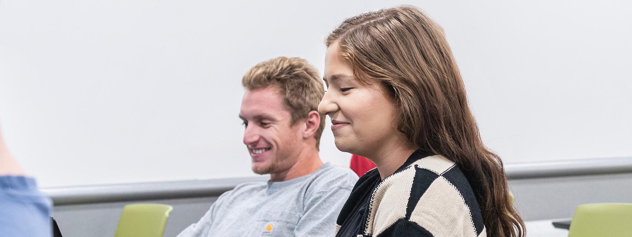 Students smile while taking notes during a class.