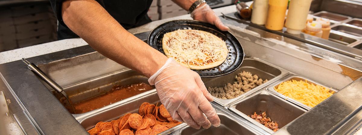 Dining services employee making a pizza.