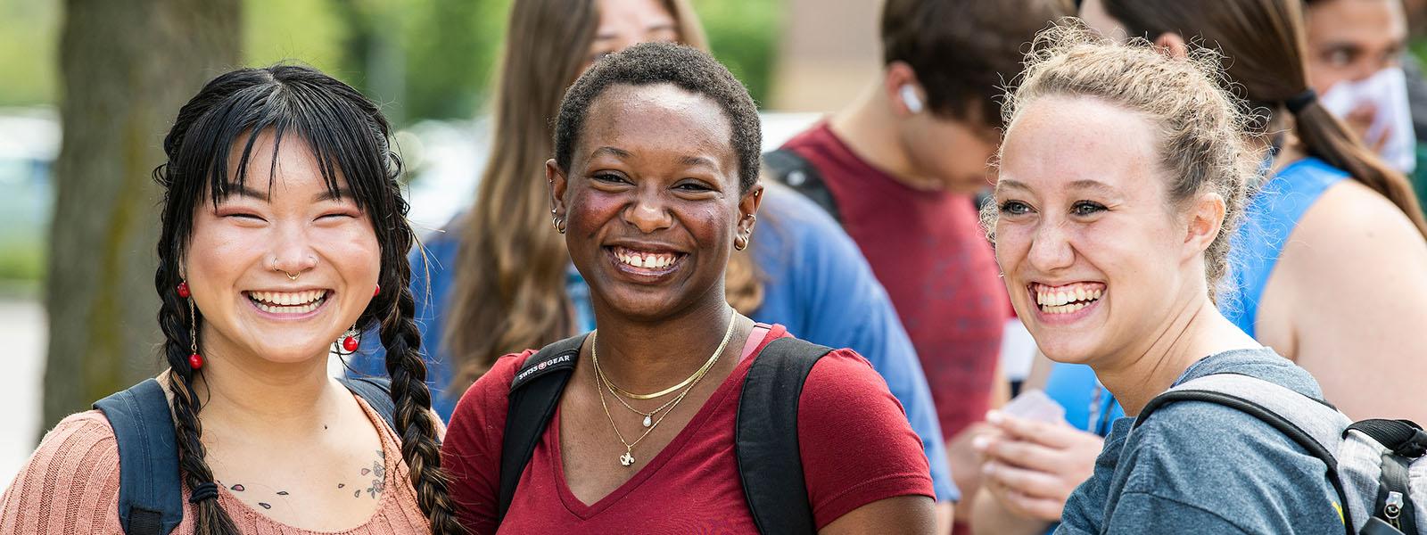 Three smiling female students at a campus BBQ.