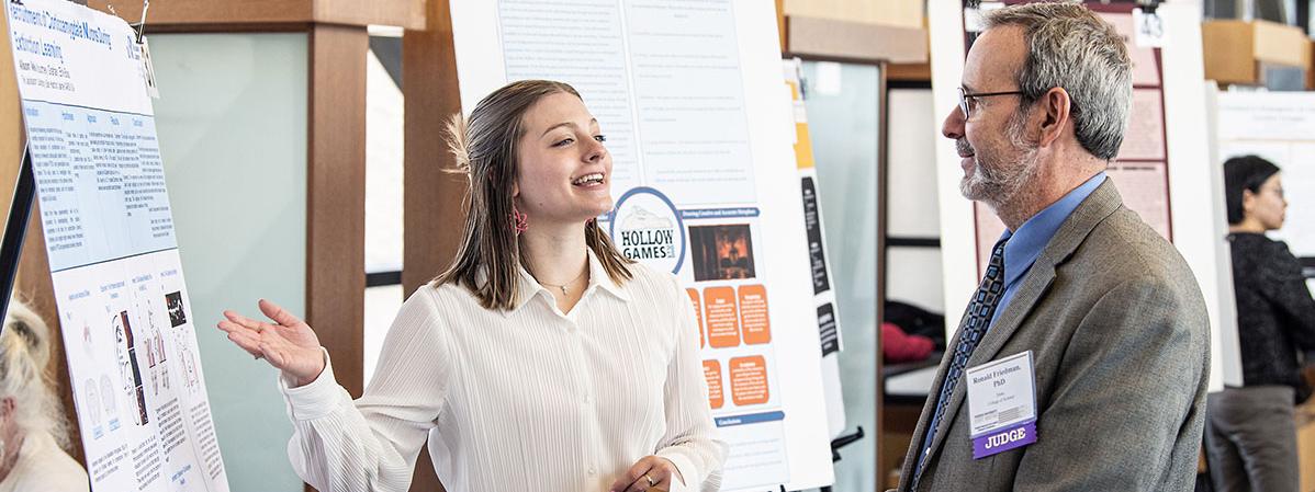A student explains her research project to a judge at the symposium