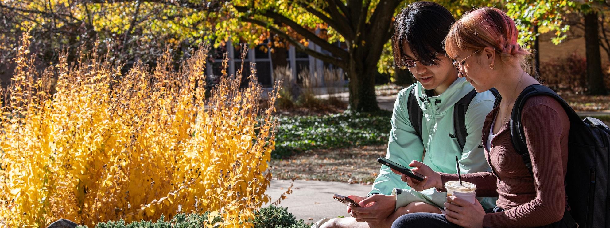 Students sitting on a bench on campus exchange phone numbers for a study session.