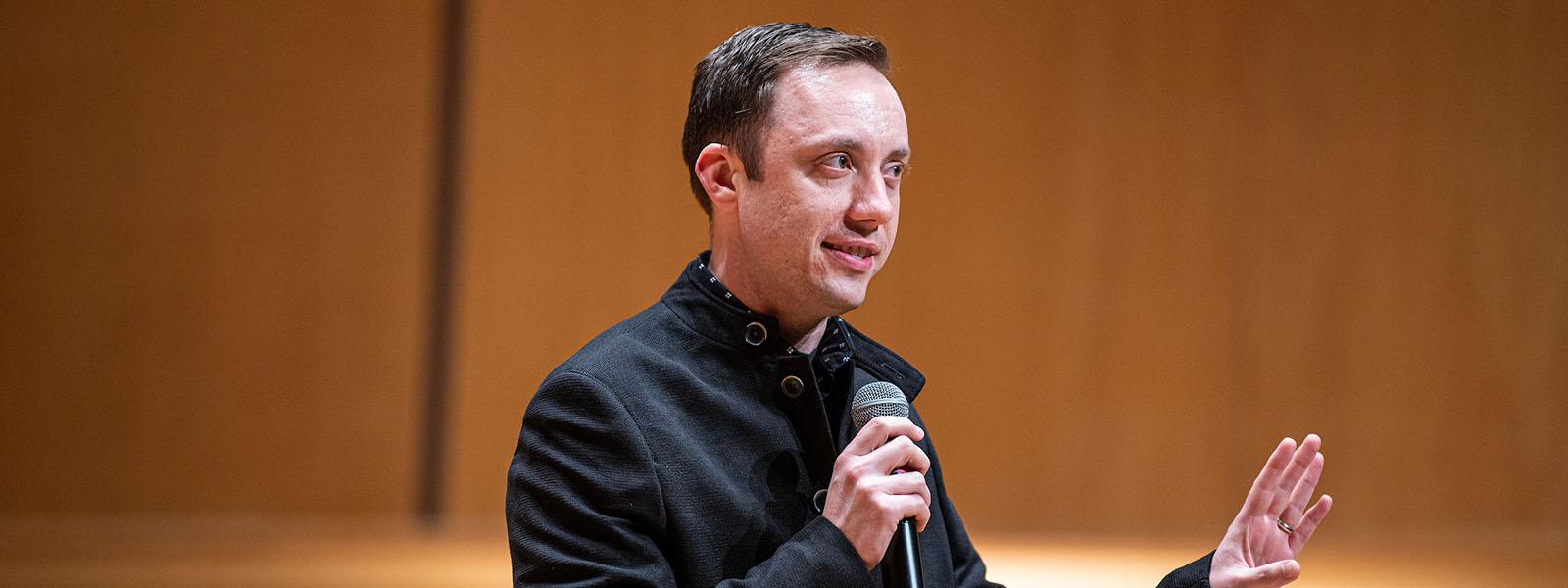 William Sauerland is onstage and speaking with a microphone