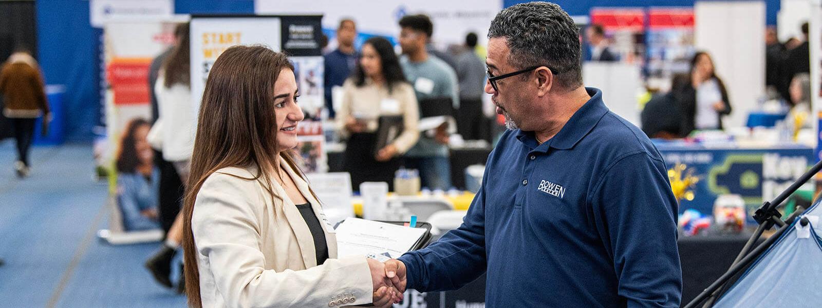 A student is shaking hands with a prospective employer at a career fair