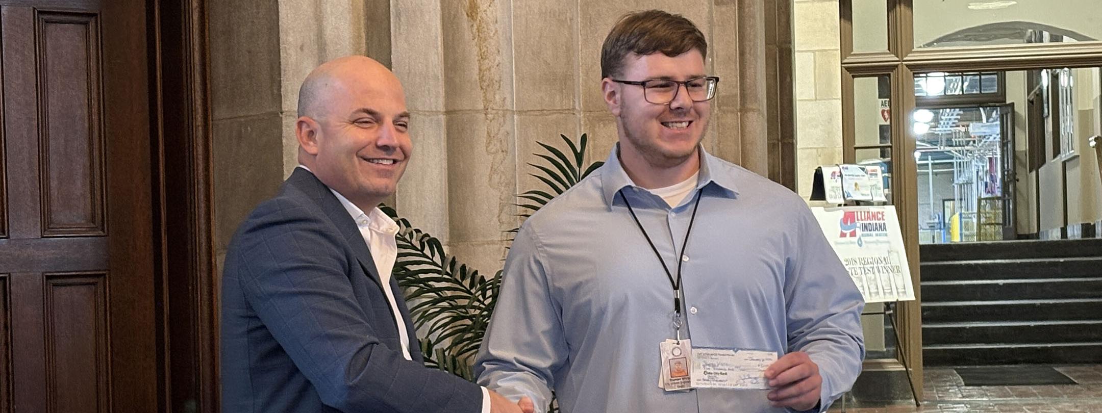 Truman Wirtz is holding a check and shaking someone's hand