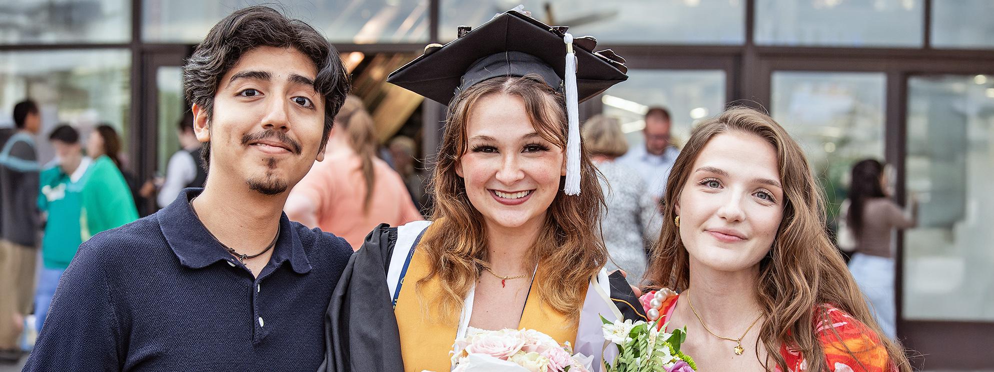 A student poses with two friends during the 2025 commencement ceremony