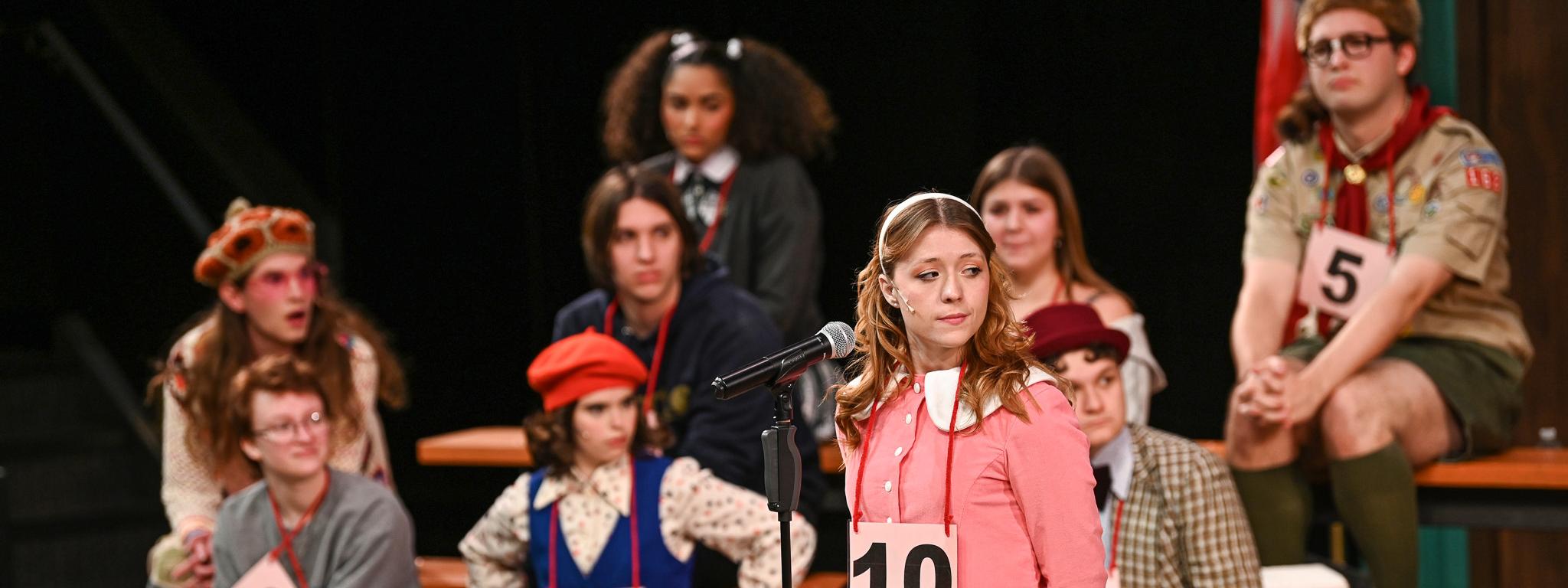Several actors on stage performing as spelling bee contestants