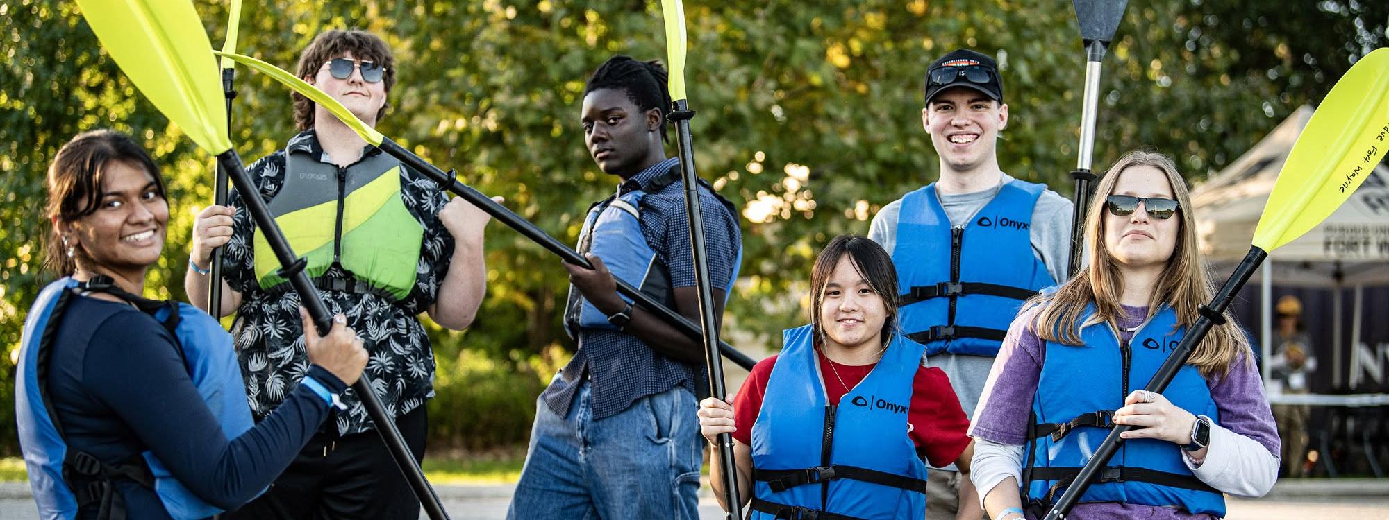 Several students are holding kayak paddles