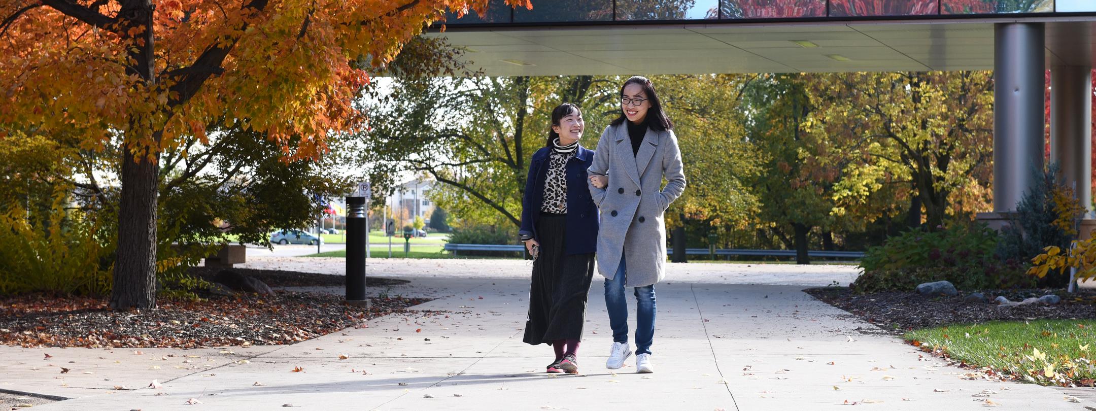 Two students walking on campus on an autumn afternoon.