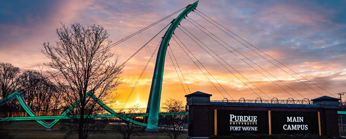 Campus sign with the bridge and a sunrise in the background.